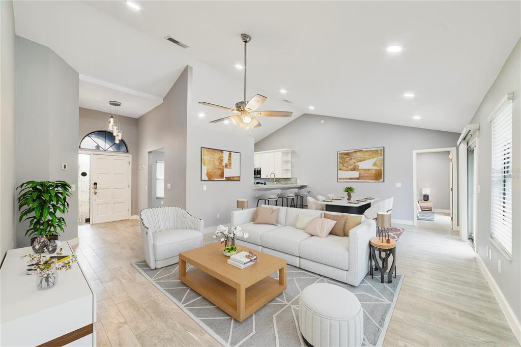 A bright, open-concept living room features vaulted ceilings, light wood-look flooring, and neutral furnishings — 515 STILLWATER DRIVE, OVIEDO, FL