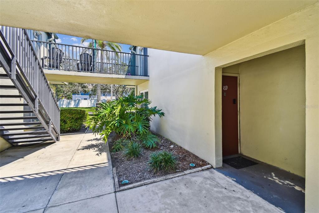 An outdoor ground-level entryway with a red door, concrete walkway, and a small garden bed — 1799 N HIGHLAND AVENUE UNIT 169, CLEARWATER, FL