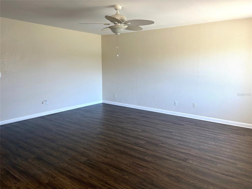 An empty room features dark wood-look flooring, beige walls, and a white ceiling fan — 2202 CLUBHOUSE DRIVE UNIT 185, SUN CITY CENTER, FL