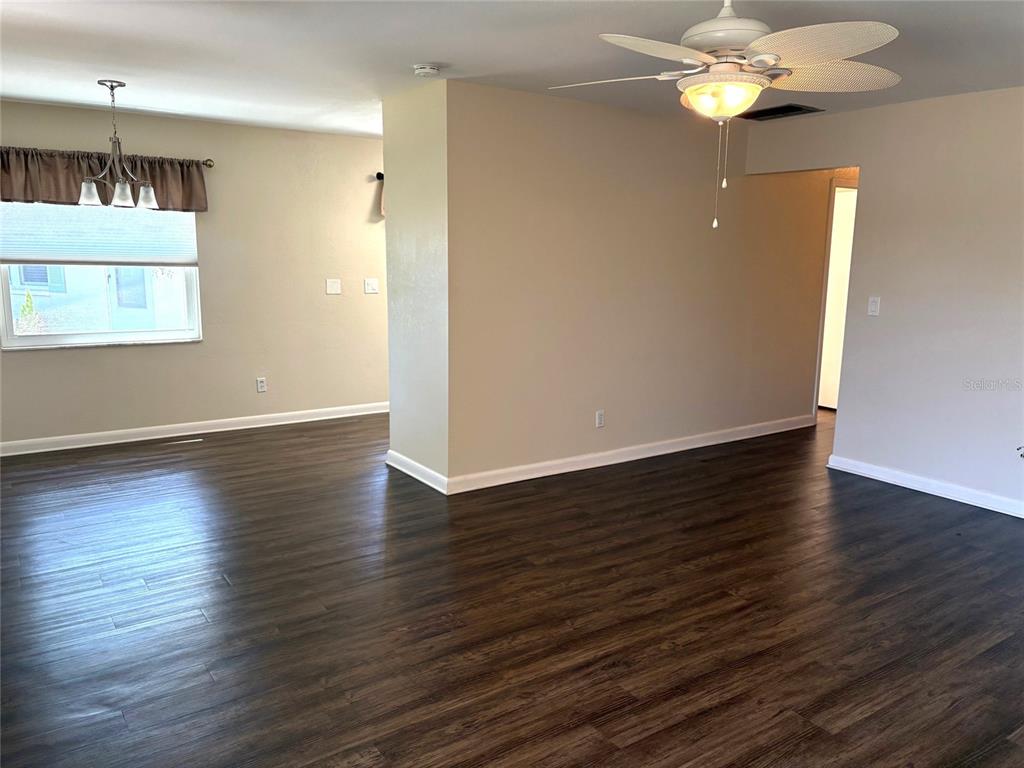 An open-concept living area features dark wood-look flooring, beige walls, and a ceiling fan — 2202 CLUBHOUSE DRIVE UNIT 185, SUN CITY CENTER, FL