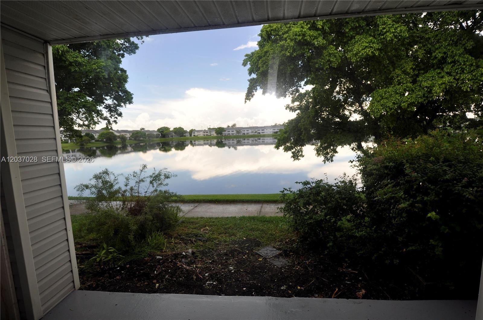 A view from a covered patio overlooking a lake and distant residential buildings — 3473 NW 44th St # 103, Oakland Park FL 33309, OAKLAND PARK, FL