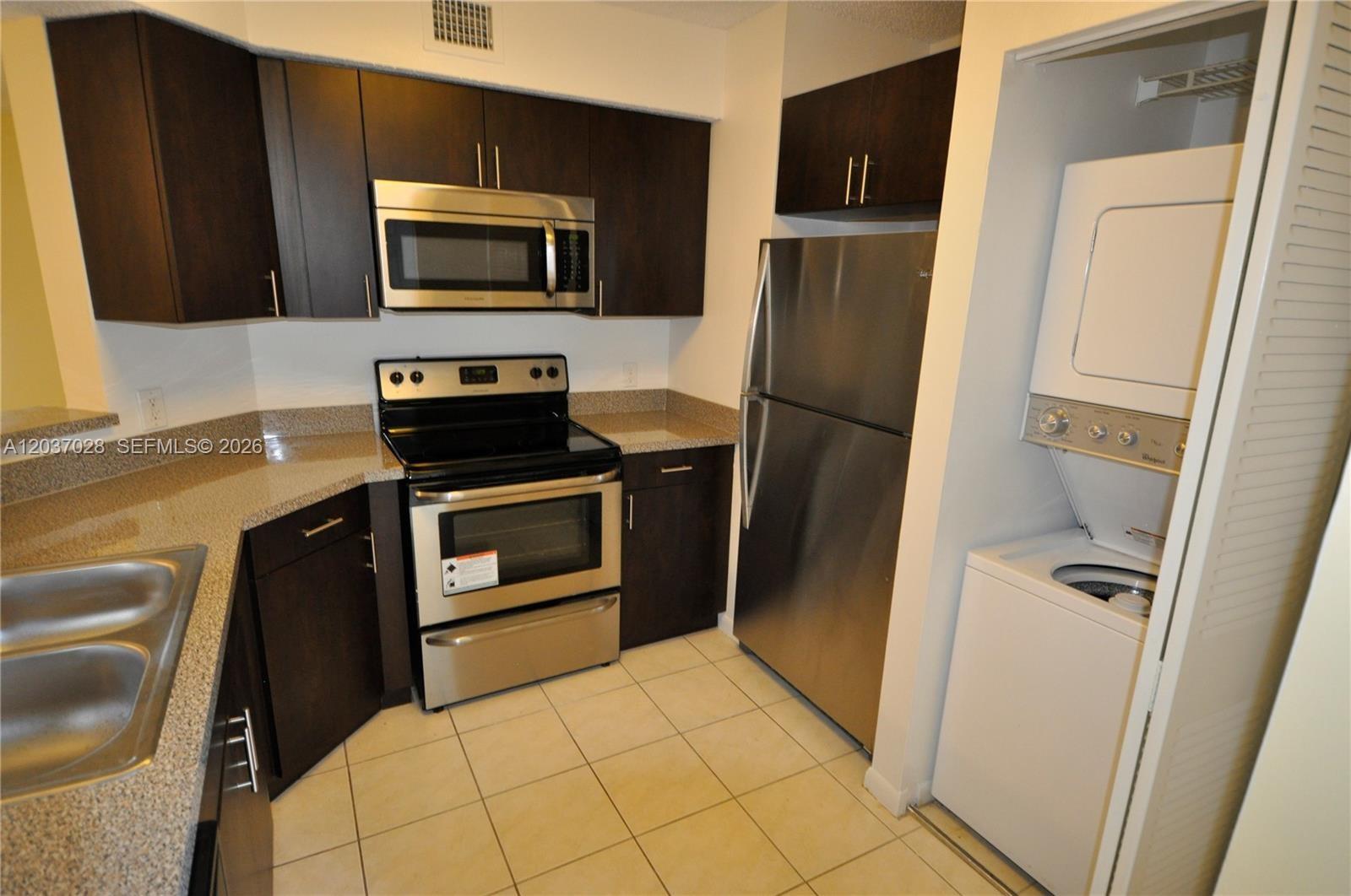 A kitchen features dark wood cabinets, stainless steel appliances, granite countertops, and a laundry closet — 3473 NW 44th St # 103, Oakland Park FL 33309, OAKLAND PARK, FL