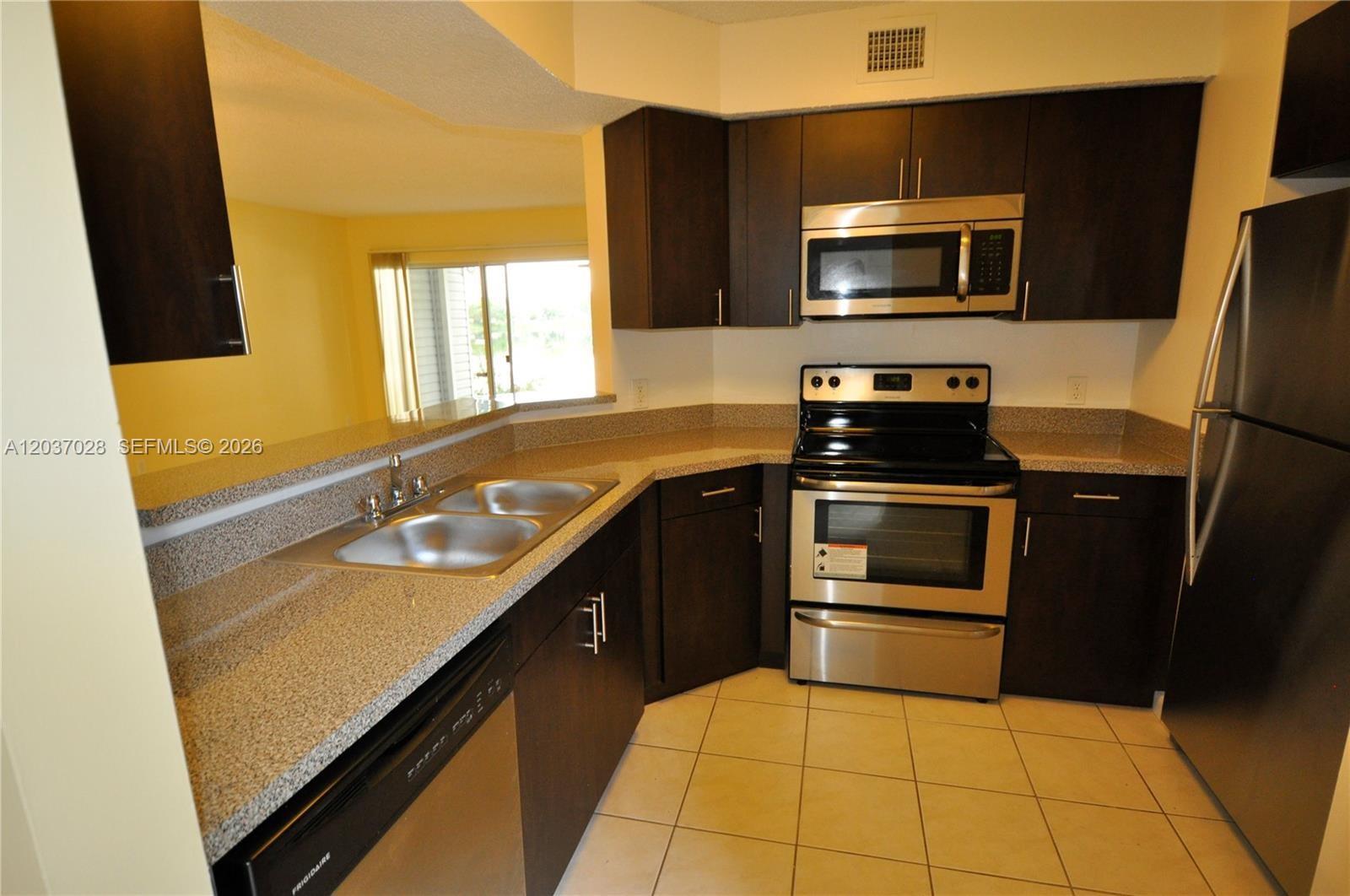 A kitchen features dark wood cabinets, stainless steel appliances, and speckled granite countertops — 3473 NW 44th St # 103, Oakland Park FL 33309, OAKLAND PARK, FL