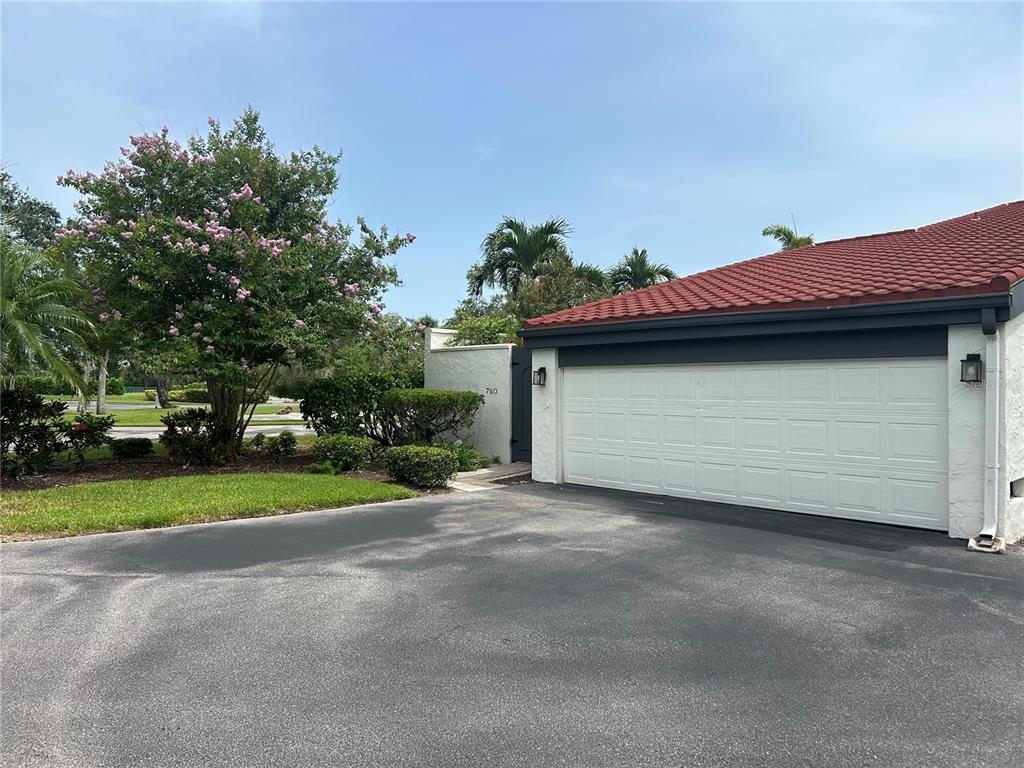 A white garage with a red tile roof sits next to a flowering tree — 780 SARABAY ROAD UNIT 16, OSPREY, FL