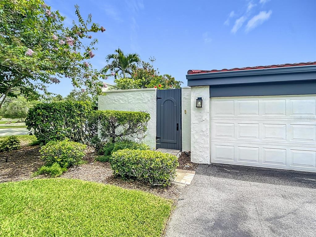 A white garage door sits next to a dark gray pedestrian gate in a stucco wall — 780 SARABAY ROAD UNIT 16, OSPREY, FL