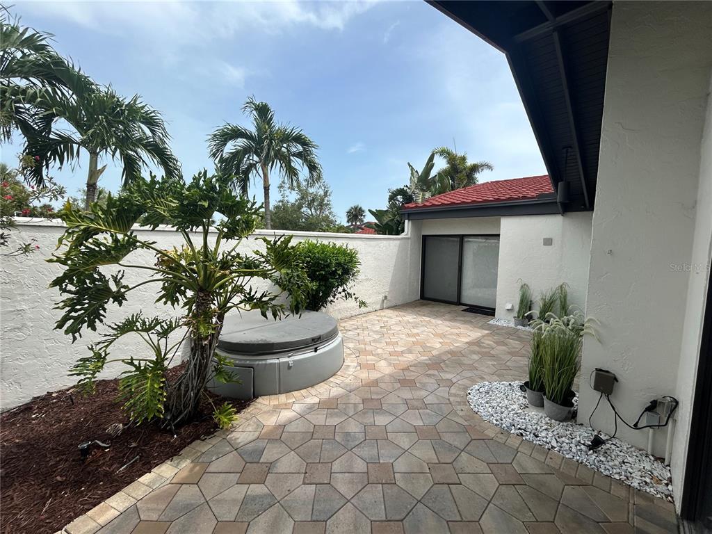 A paved patio features a hot tub, a large tropical plant, and a white privacy wall — 780 SARABAY ROAD UNIT 16, OSPREY, FL