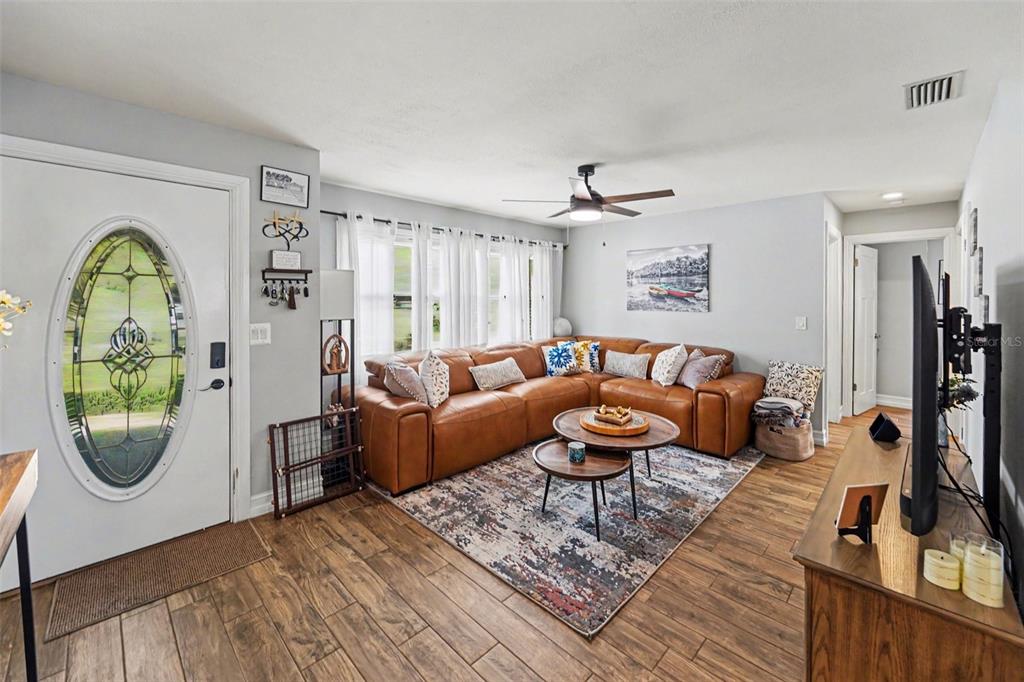 A living room features a brown leather sectional, a patterned area rug, and wood-look flooring — 3369 HUNT CLUB DRIVE, CLEARWATER, FL