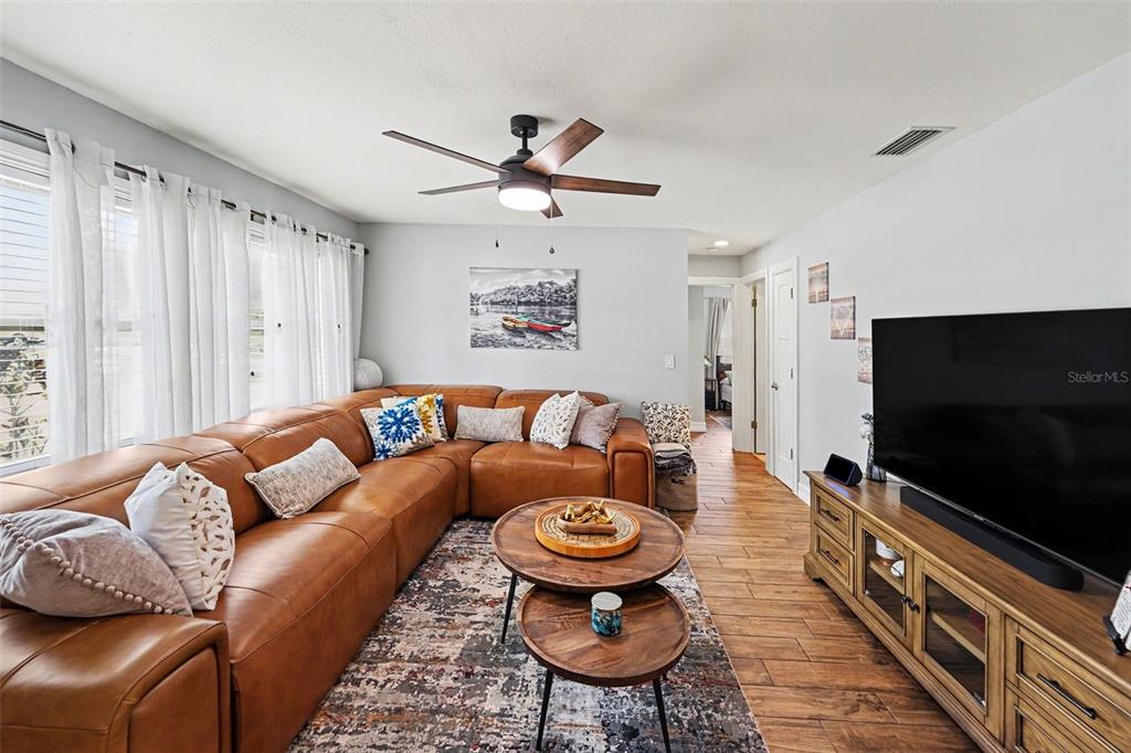 A living room features a large brown leather sectional, wood-look tile flooring, and a television — 3369 HUNT CLUB DRIVE, CLEARWATER, FL