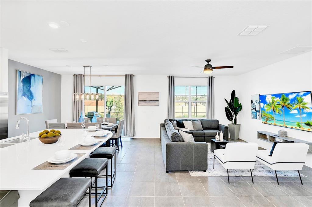An open-concept living and dining area features a kitchen island, gray sofa, and television — 234 MARCELLO BOULEVARD, KISSIMMEE, FL