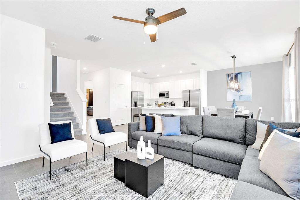 A modern open-concept living room features a gray sectional sofa, two white chairs, and kitchen — 234 MARCELLO BOULEVARD, KISSIMMEE, FL