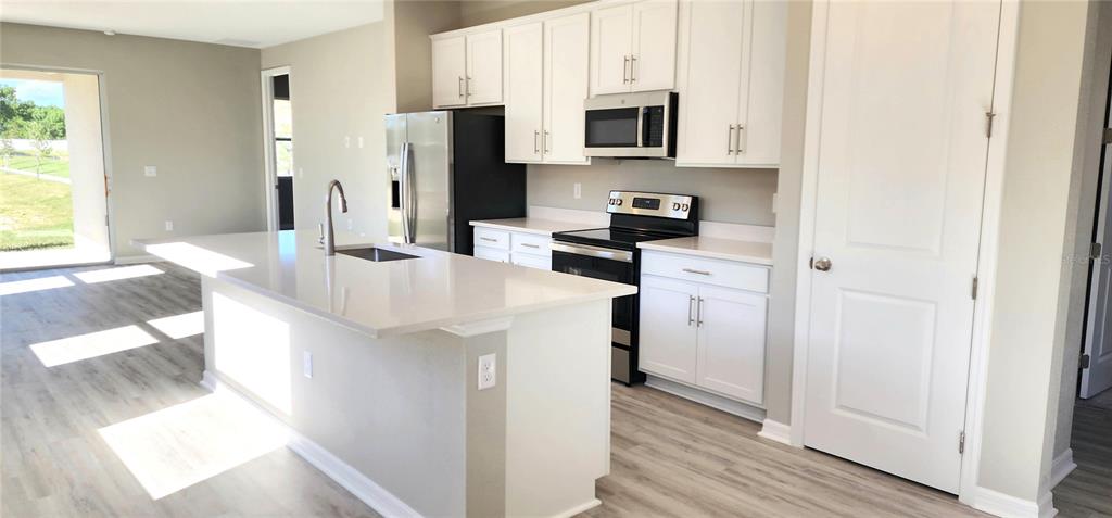 A modern kitchen with white cabinets and quartz countertops overlooks an open-concept living area — 932 BLUE CREEK DRIVE, HAINES CITY, FL