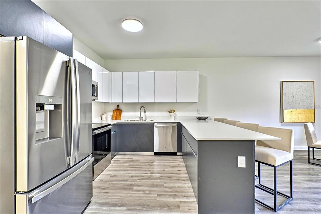 A modern kitchen features dark lower cabinets, white upper cabinets, stainless appliances, and a breakfast bar — 1595 NW 29TH ROAD UNIT 3, GAINESVILLE, FL