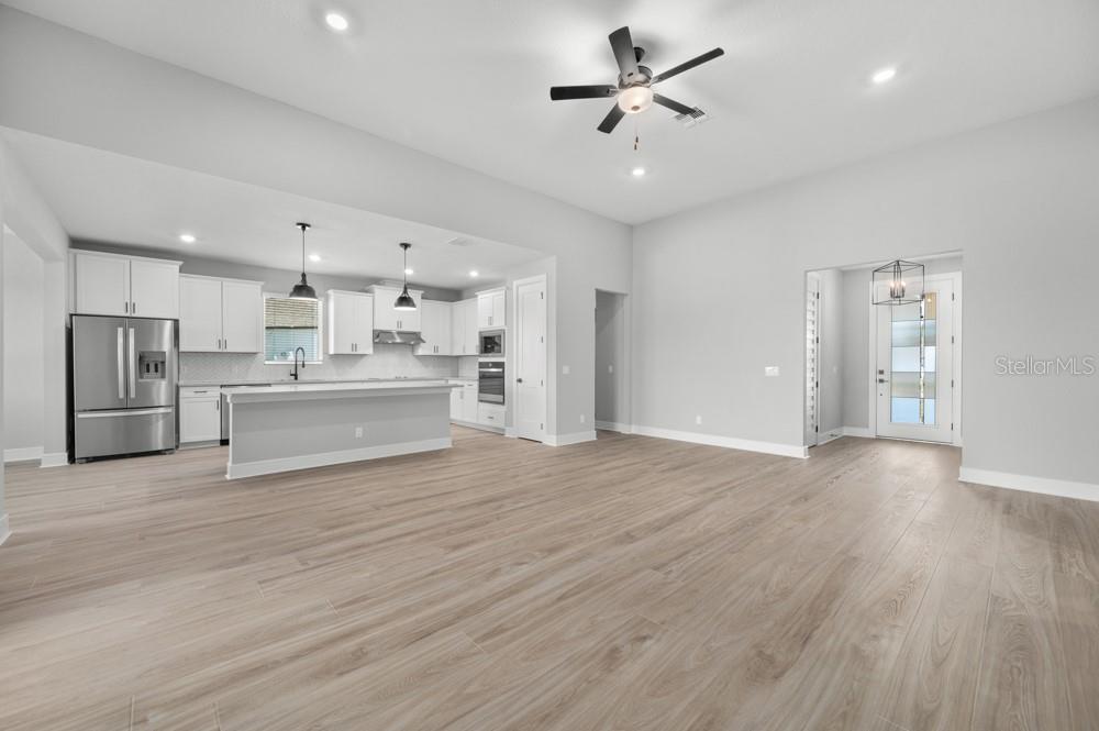 An open-concept living area with light wood-look flooring, a kitchen island, and a ceiling fan — 3849 SADDLE HILL TRAIL, FRUITLAND PARK, FL
