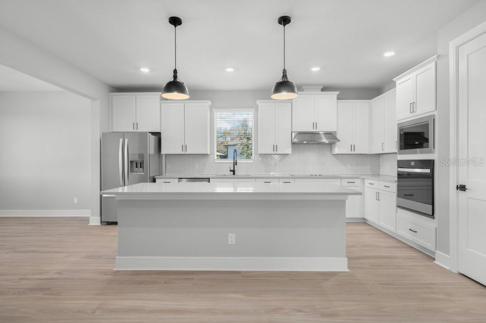 A modern kitchen features white cabinetry, a large central island, stainless steel appliances, and wood flooring — 3849 SADDLE HILL TRAIL, FRUITLAND PARK, FL