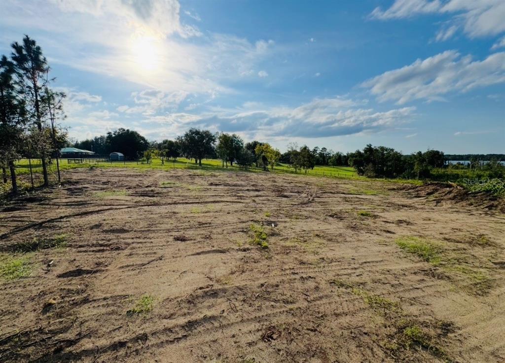 A wide, cleared dirt lot features tire tracks under a bright, partly cloudy sky — 16865 SE 27TH PLACE ROAD, OCKLAWAHA, FL