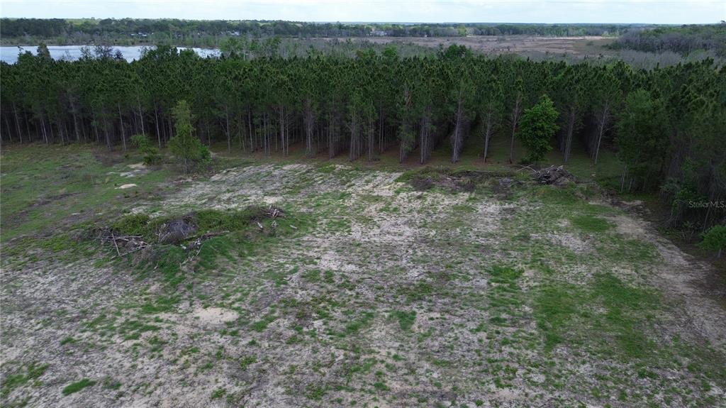 An aerial view shows a cleared, sandy lot bordered by a dense forest and a lake — 16865 SE 27TH PLACE ROAD, OCKLAWAHA, FL
