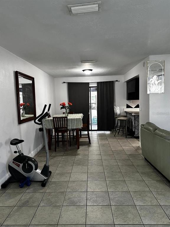 A dining area with a table, exercise bike, and tile flooring leads to a sliding door — 1048 WAKEFIELD CIRCLE, DELTONA, FL