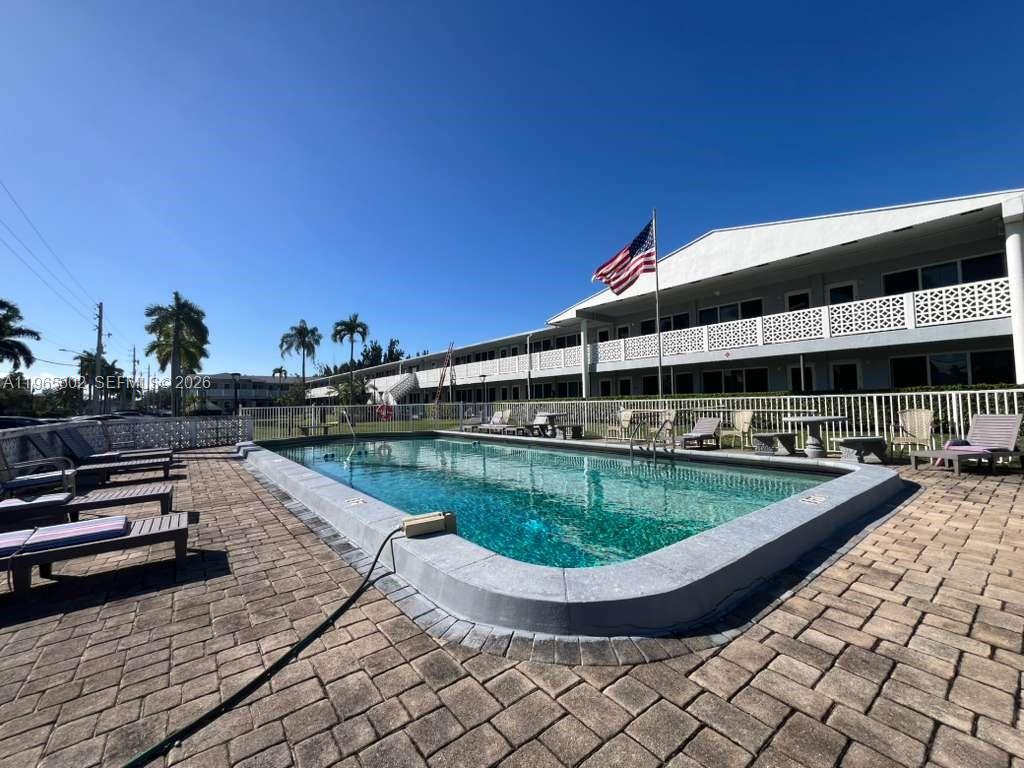 An outdoor swimming pool with lounge chairs sits in front of a two-story apartment building — 600 Layne Blvd # 110, Hallandale Beach FL 33009, HALLANDALE BEACH, FL