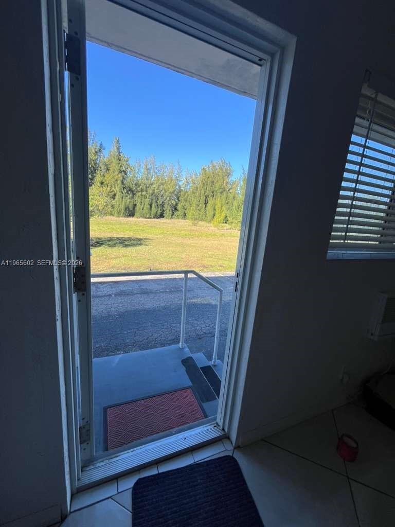 A view through an open glass door shows a small concrete porch and grassy field — 600 Layne Blvd # 110, Hallandale Beach FL 33009, HALLANDALE BEACH, FL