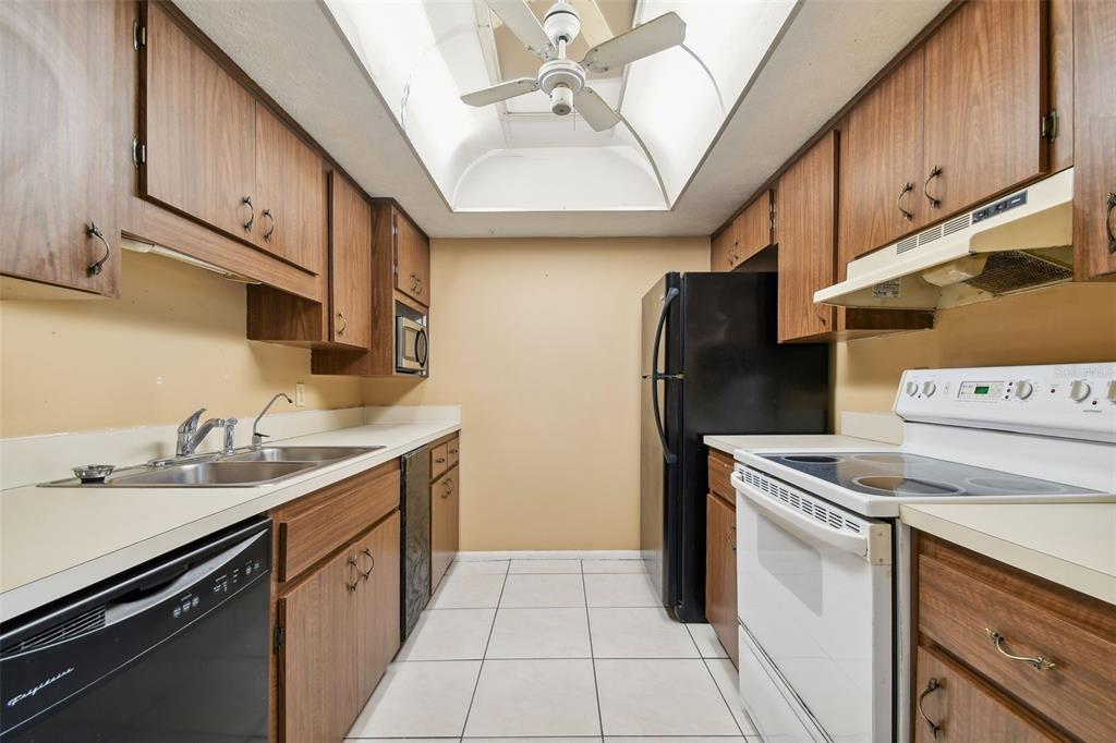 A galley kitchen features wood cabinets, white countertops, a black dishwasher, and a black refrigerator — 645 N KEENE ROAD UNIT D, CLEARWATER, FL