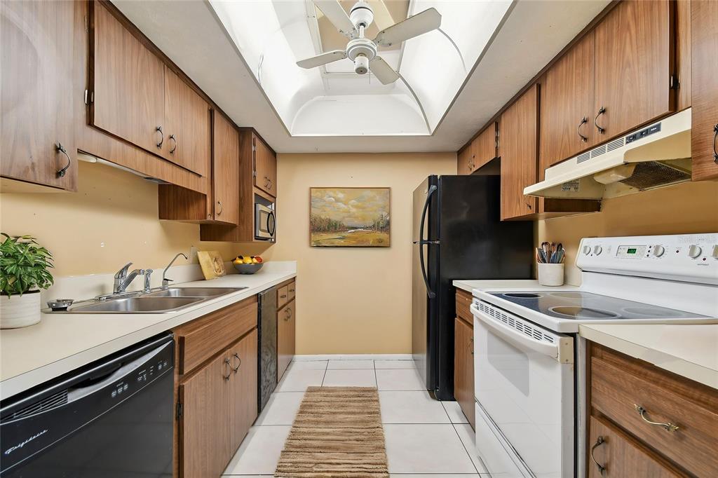 A galley kitchen features wood cabinets, white countertops, a black refrigerator, and a white stove — 645 N KEENE ROAD UNIT D, CLEARWATER, FL