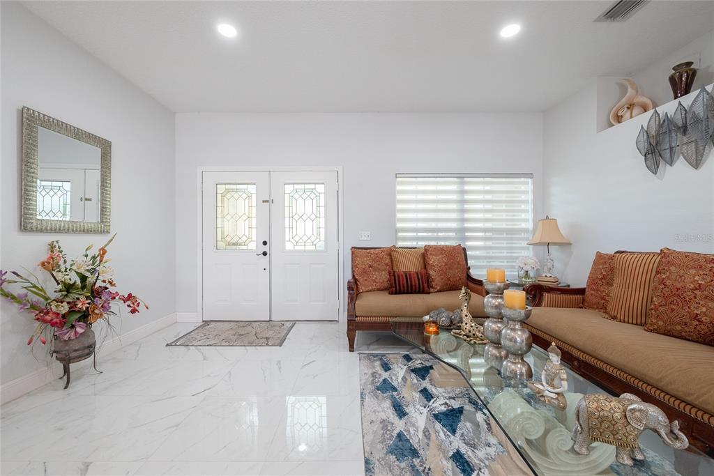 A bright living room features white marble floors, a double front door, and traditional furniture — 3200 VICTORIA DRIVE, KISSIMMEE, FL