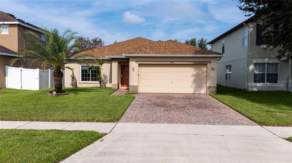 A single-story house with a tan stucco exterior, a brown shingled roof, and a paver driveway — 2808 POLSON DRIVE, KISSIMMEE, FL