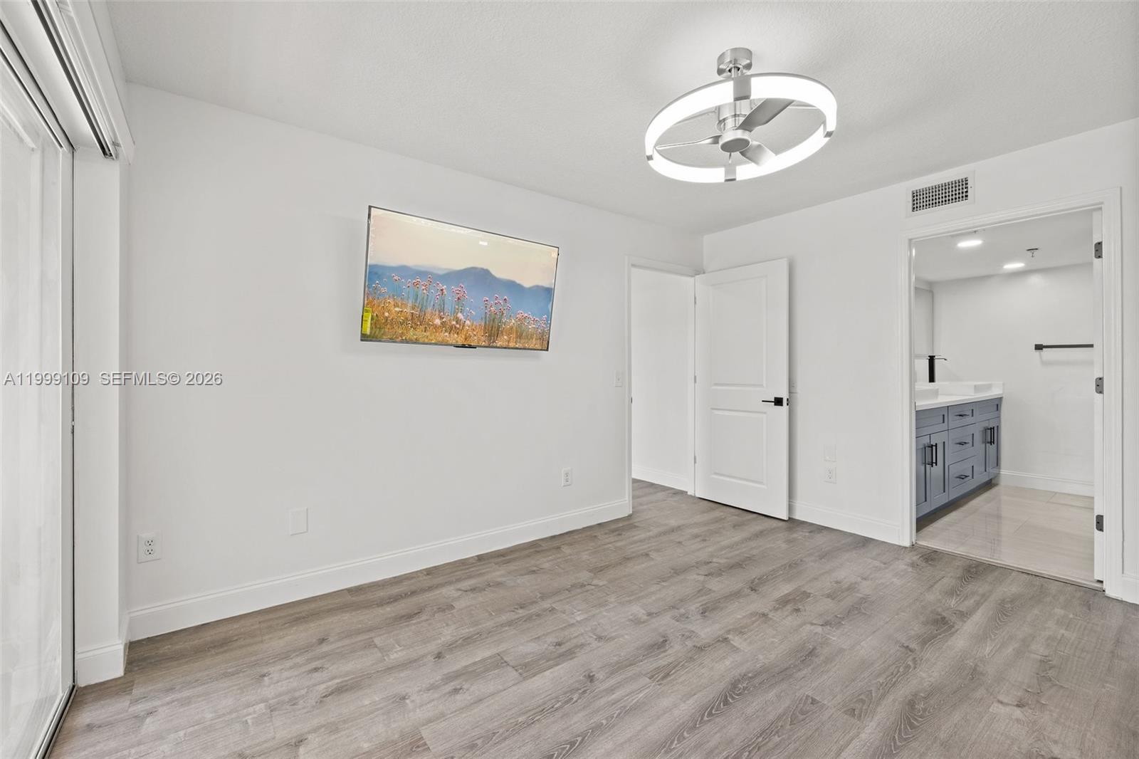 A bedroom features white walls, gray wood-look flooring, a wall-mounted television, and an attached bathroom — 470 S Park Rd # 307, Hollywood FL 33021, HOLLYWOOD, FL