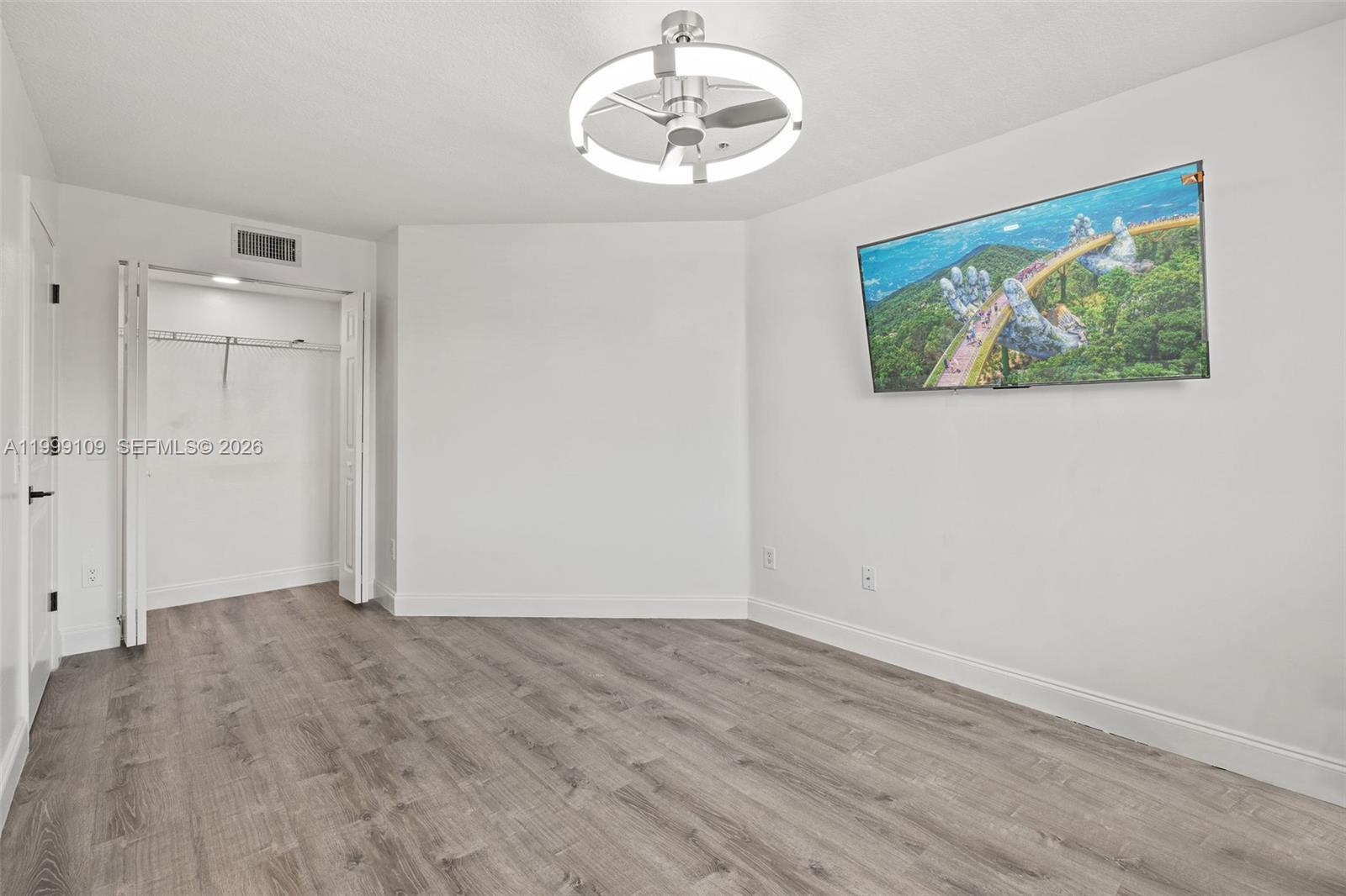 A bedroom features light wood-look flooring, a ceiling fan with integrated lighting, and a wall-mounted television — 470 S Park Rd # 307, Hollywood FL 33021, HOLLYWOOD, FL