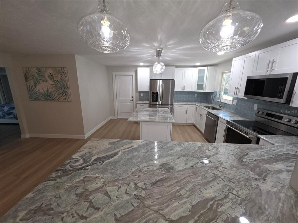 A kitchen features white cabinets, marble-patterned countertops, stainless steel appliances, and three glass pendant lights — 63 OAKWOOD DRIVE, DUNEDIN, FL