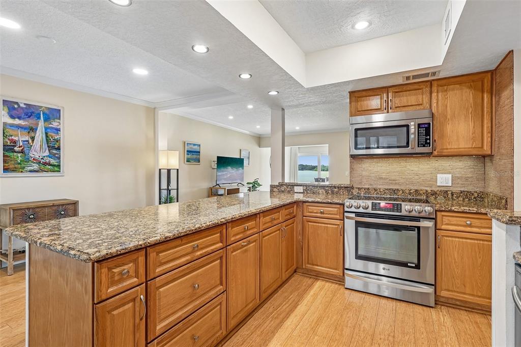 A kitchen with wood cabinets, granite countertops, and stainless steel appliances overlooks a living area — 632 DESOTO DRIVE UNIT 632, CASSELBERRY, FL