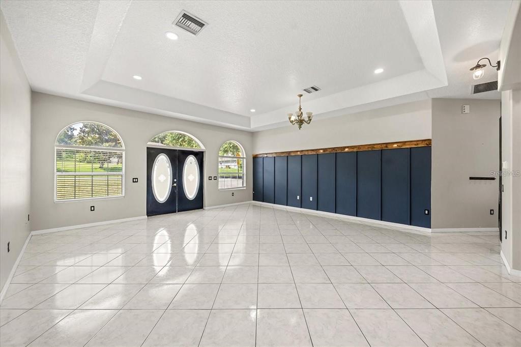A spacious room features white tile floors, a tray ceiling, and a dark blue paneled wall — 13848 VISTA DEL LAGO BOULEVARD, CLERMONT, FL