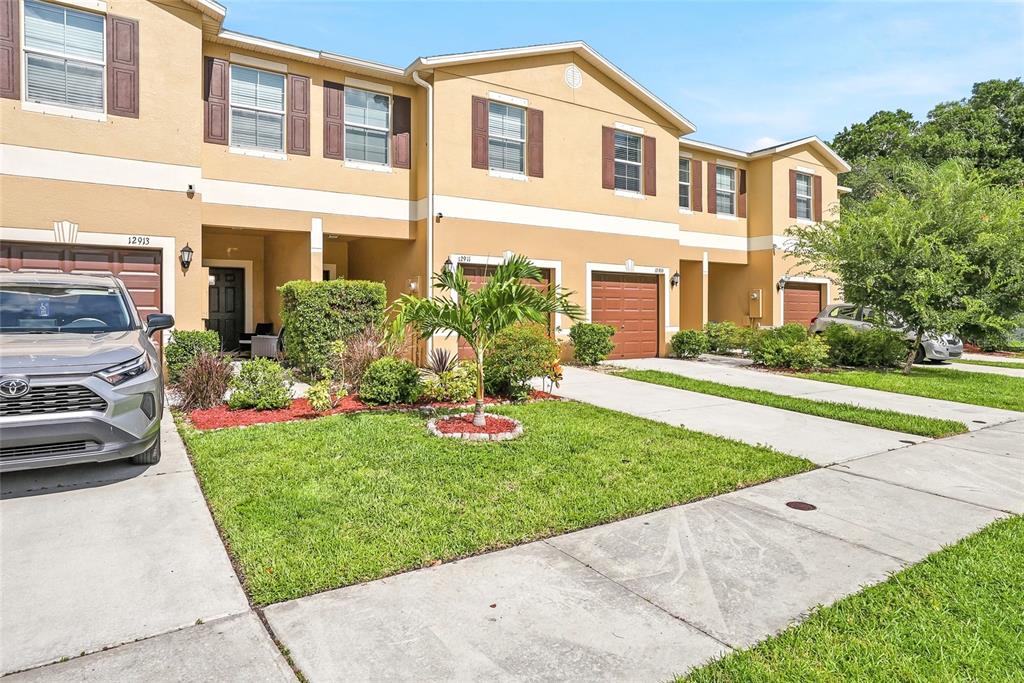 A row of two-story townhomes with tan stucco exteriors, brown garage doors, and landscaped front yards — 12911 DREAM CATCHER WAY, RIVERVIEW, FL