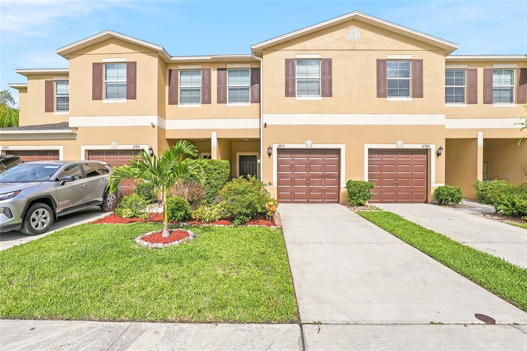 A row of tan two-story townhouses with brown garage doors and a shared front lawn — 12911 DREAM CATCHER WAY, RIVERVIEW, FL
