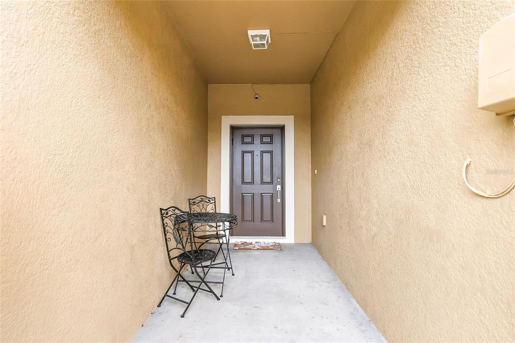 A covered entryway features a brown front door, light-colored stucco walls, and a small bistro set — 12911 DREAM CATCHER WAY, RIVERVIEW, FL