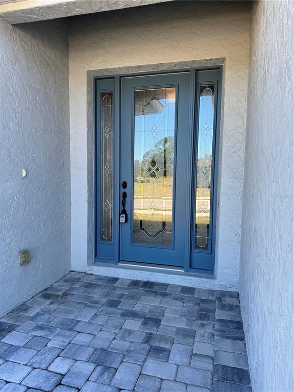 A blue front door with glass panels and sidelights sits on a paved entryway — 720 REDBUD COURT, ENGLEWOOD, FL