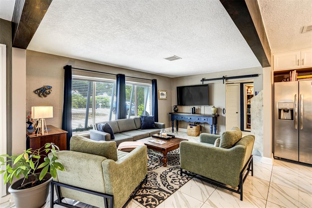 A living room features a grey sofa, two green armchairs, a television, and tile flooring — 326 MEHLENBACHER ROAD, BELLEAIR, FL