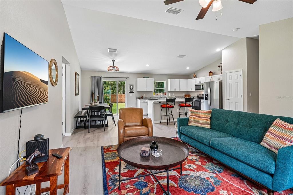 An open-concept living room and kitchen featuring a teal sofa, leather chair, and dining area — 9971 N BAMBOO WAY, DUNNELLON, FL