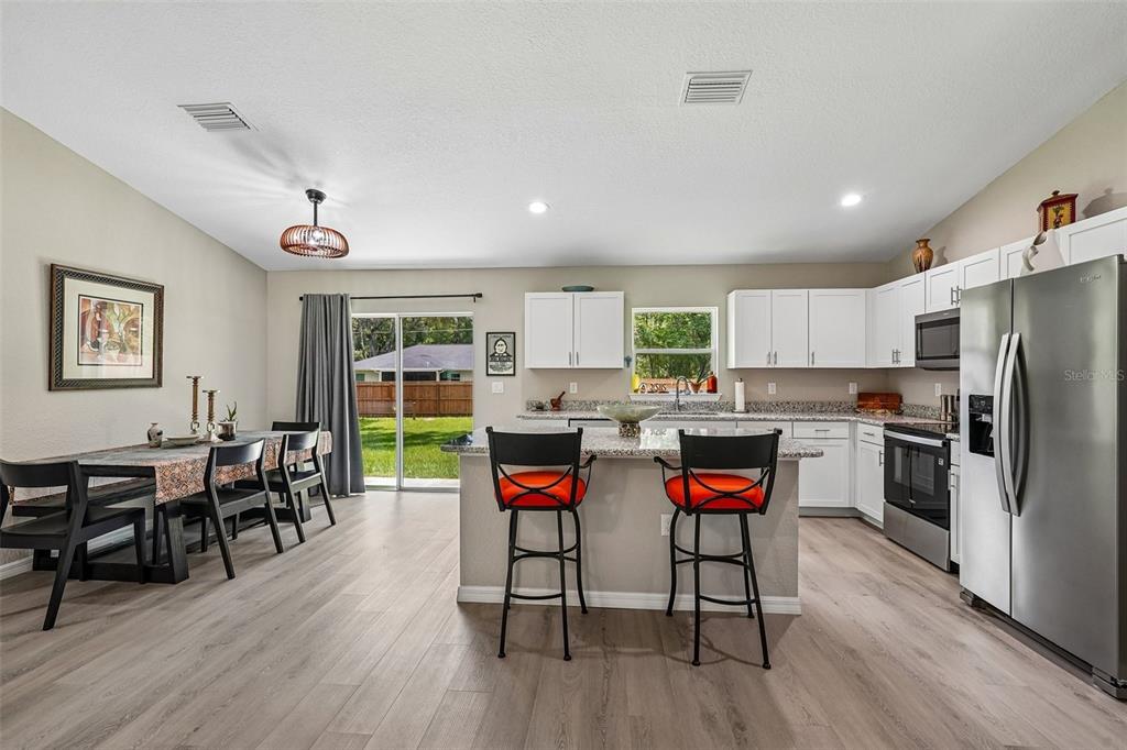 A kitchen and dining area with white cabinets, a granite island, and wood-look flooring — 9971 N BAMBOO WAY, DUNNELLON, FL