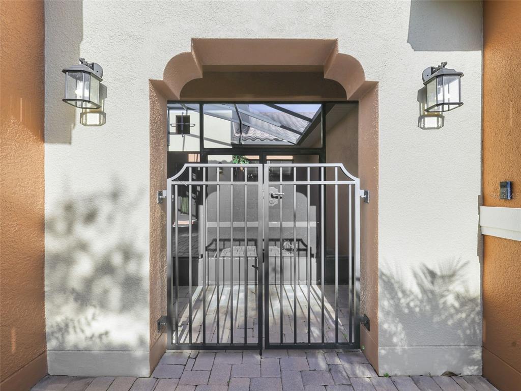 A metal gate stands within a stucco entryway featuring two wall-mounted outdoor lanterns — 619 TAPATIO LANE, KISSIMMEE, FL
