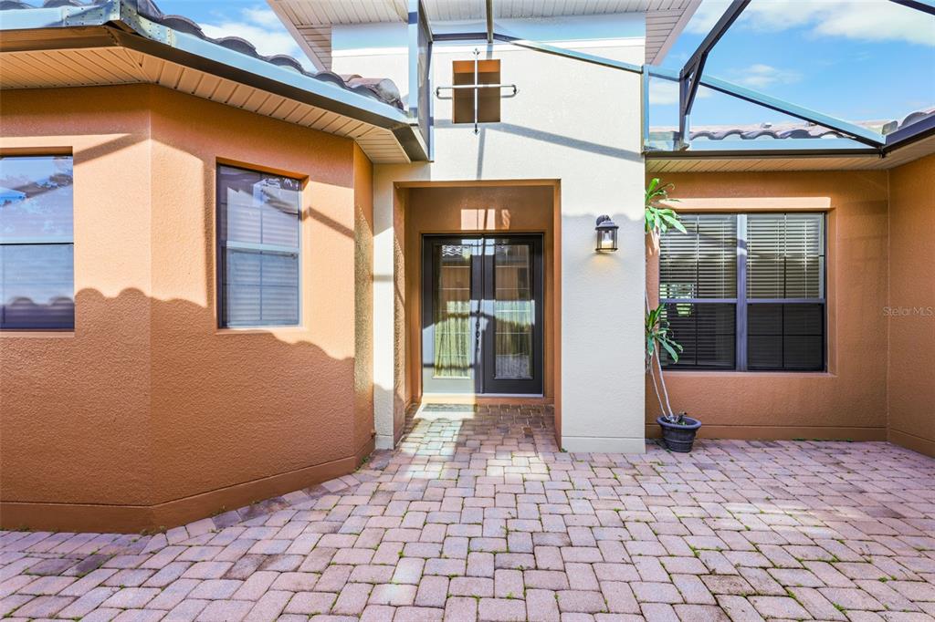 A paved courtyard leads to the double glass front doors of a stucco house — 619 TAPATIO LANE, KISSIMMEE, FL
