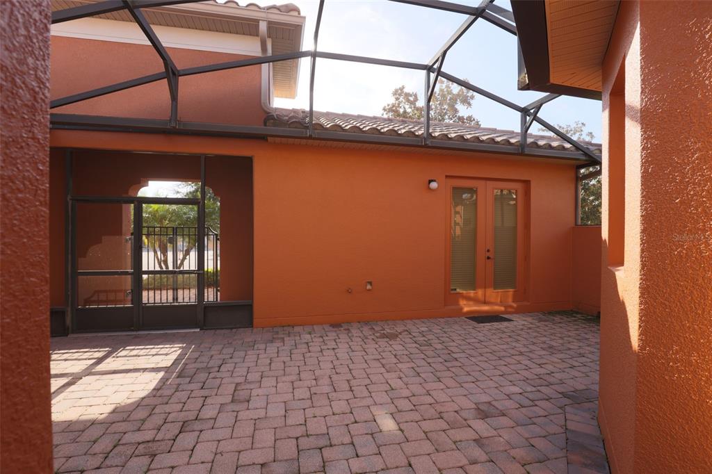A screened-in patio with brick pavers, orange stucco walls, and a set of double doors — 619 TAPATIO LANE, KISSIMMEE, FL