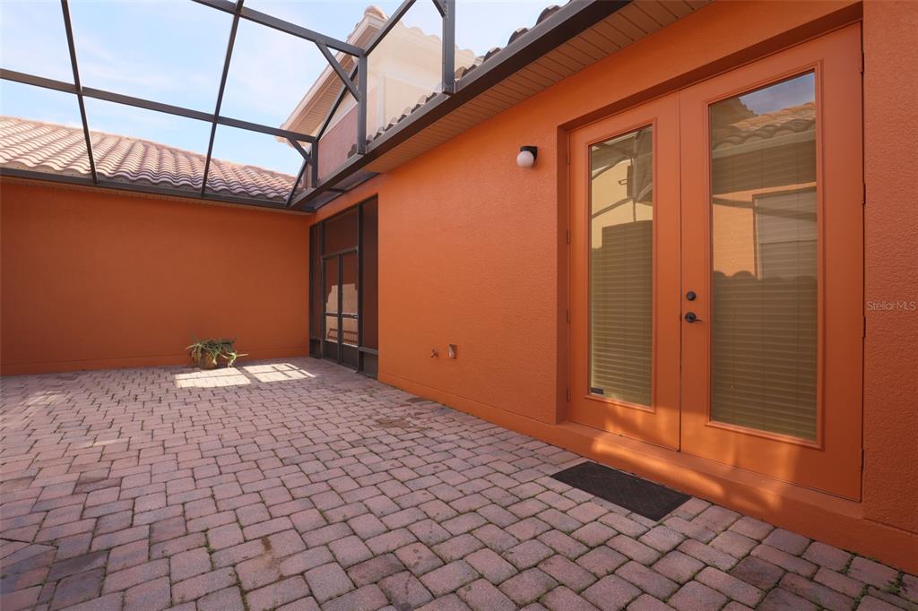 A paved patio enclosed by a screen cage features orange walls and double glass doors — 619 TAPATIO LANE, KISSIMMEE, FL