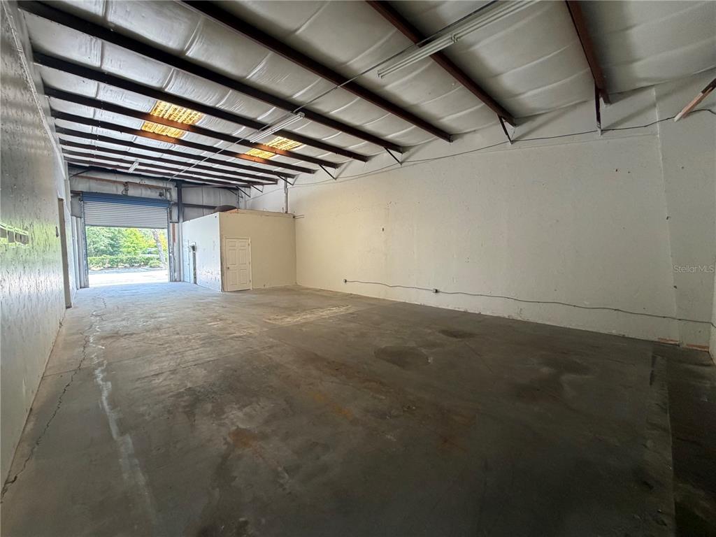 An empty industrial warehouse space features a concrete floor, white walls, and a roll-up door — 1424 HAMLIN AVENUE UNIT H, ST CLOUD, FL