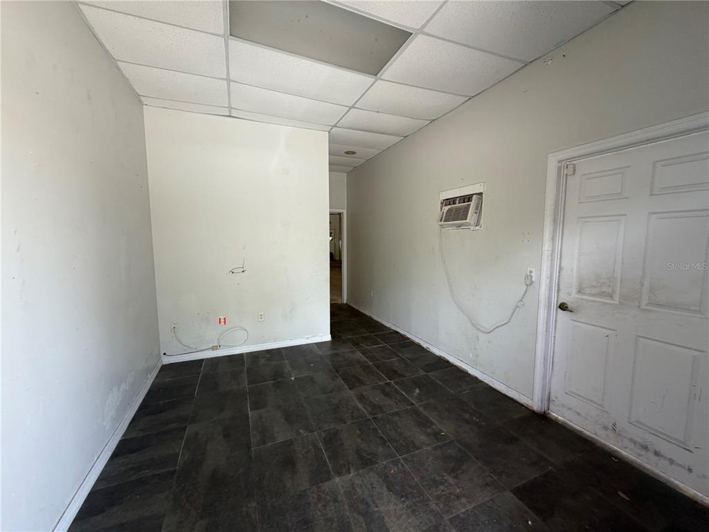 An empty room features dark tile flooring, white walls, a drop ceiling, and a door — 1424 HAMLIN AVENUE UNIT H, ST CLOUD, FL