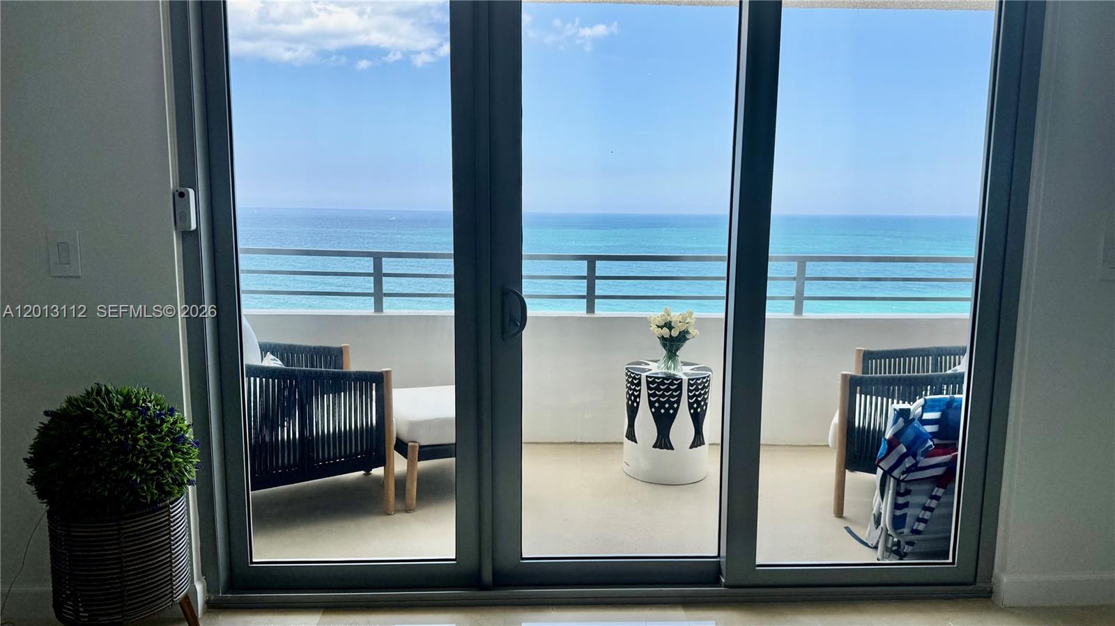 A balcony with two chairs and a small table overlooks the ocean through glass doors — 5555 Collins Ave # 14E, Miami Beach FL 33140, MIAMI BEACH, FL