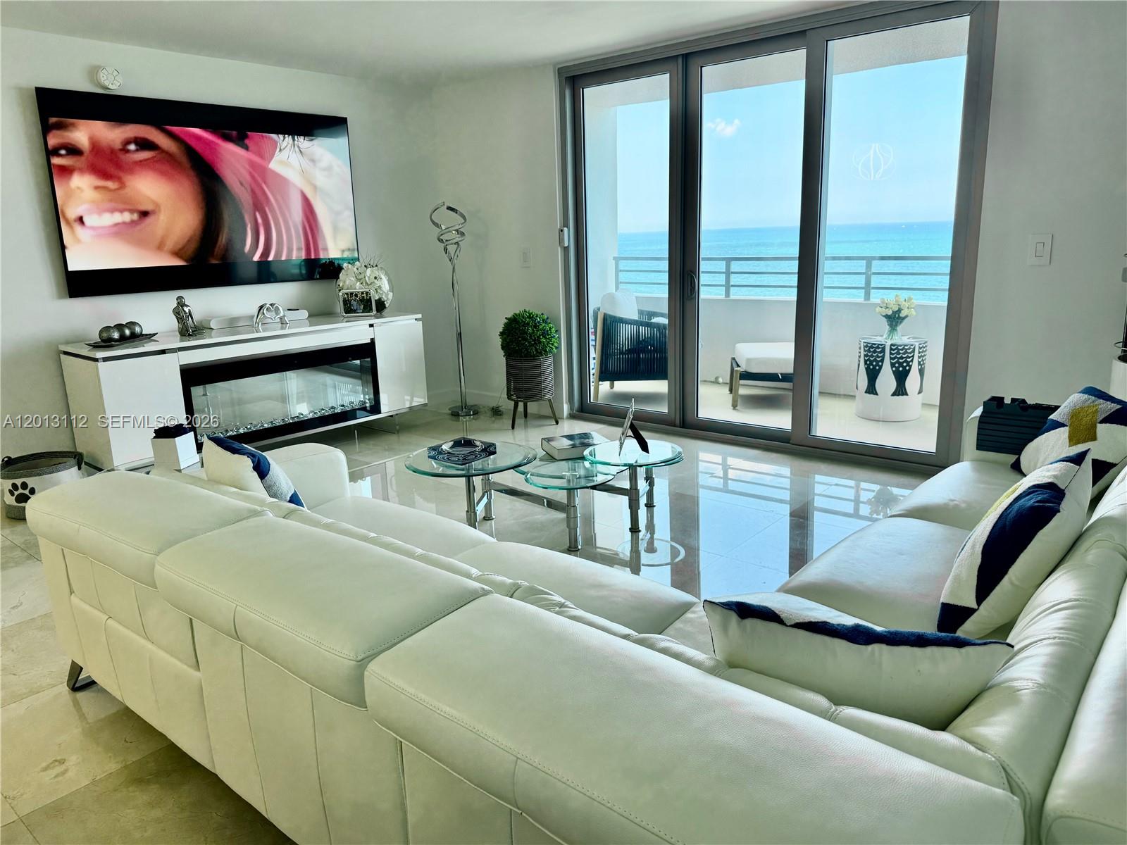 A white living room features a large sectional sofa, glass coffee tables, and ocean views — 5555 Collins Ave # 14E, Miami Beach FL 33140, MIAMI BEACH, FL