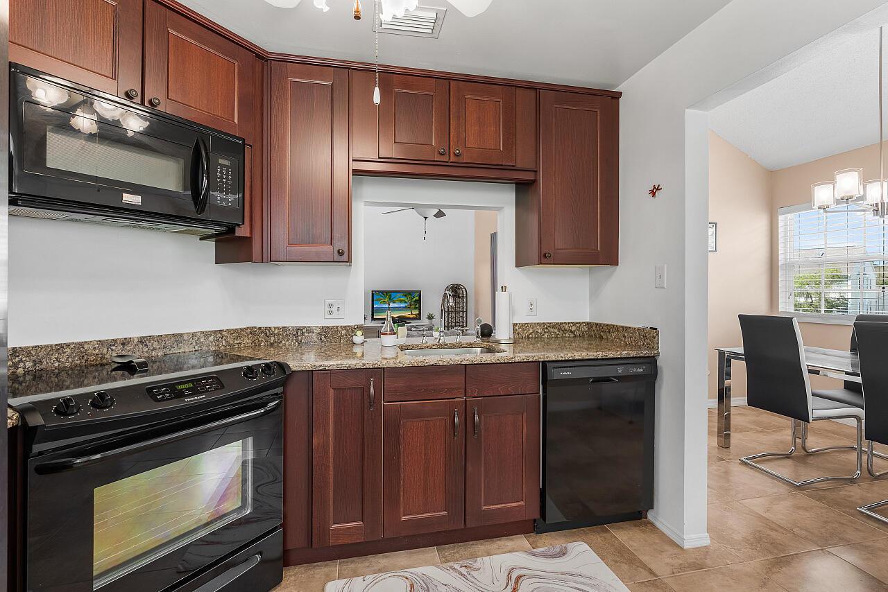 A kitchen with dark wood cabinets, black appliances, granite countertops, and a pass-through window — 1965 Westminster Circle # 6, Vero Beach FL 32966, VERO BEACH, FL