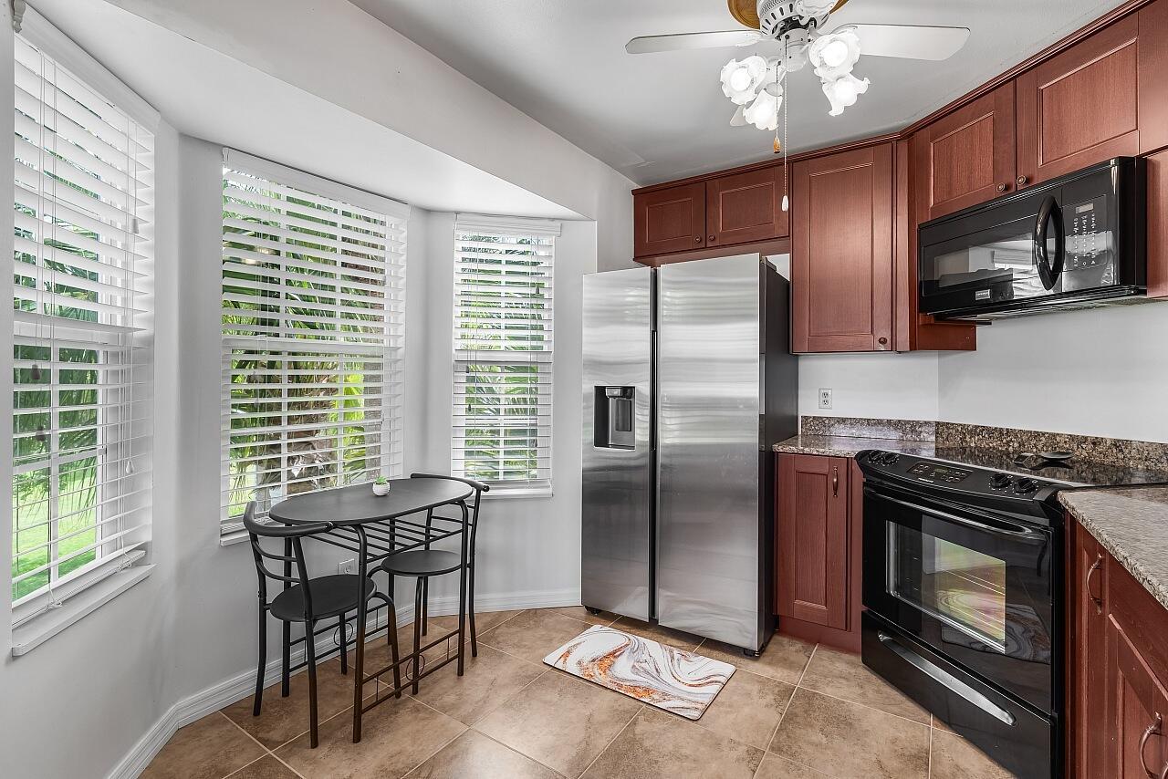 A kitchen features stainless steel appliances, dark wood cabinets, granite countertops, and a small dining nook — 1965 Westminster Circle # 6, Vero Beach FL 32966, VERO BEACH, FL