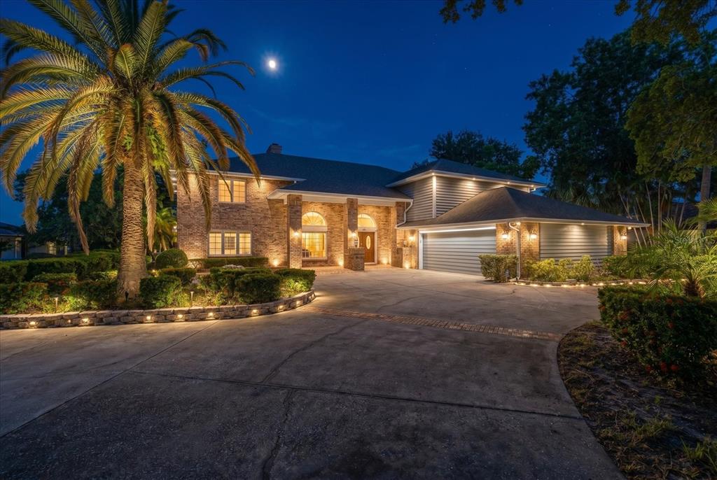 A two-story brick house with a palm tree, driveway, and garage at night — 220 HARBOR VIEW LANE, LARGO, FL